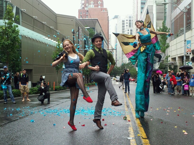 A couple dancing on the street with a stilt-walker throwing confetti