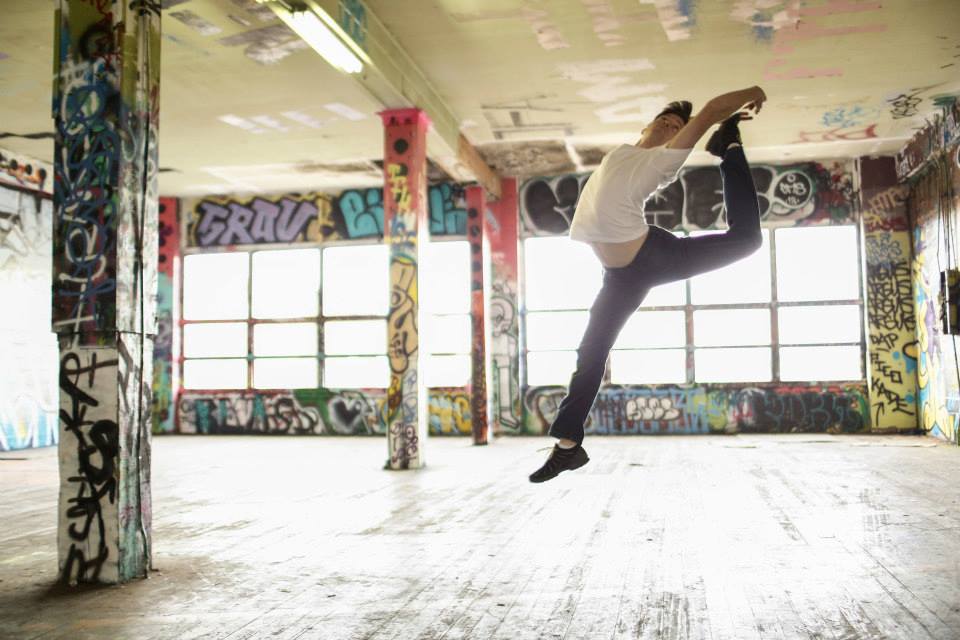 Still of Jared leaping in the air in an abandoned building with graffiti on the walls
